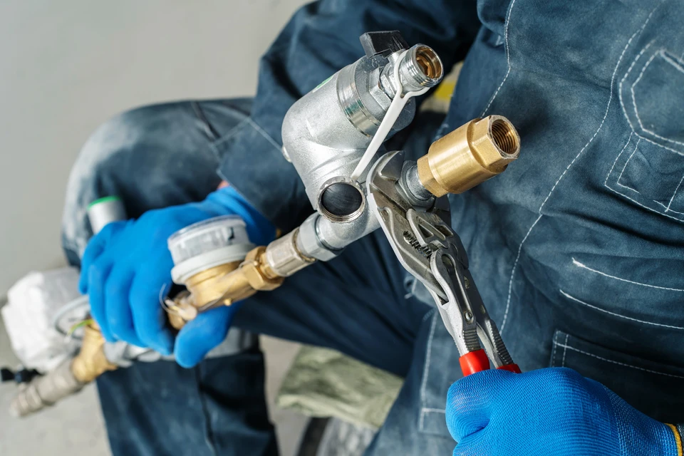 Technicien en combinaison bleue manipulant des raccords hydrauliques avec gants de protection