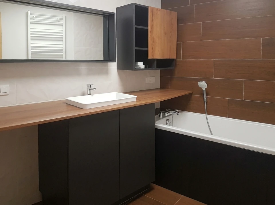 Photographie réaliste en plan large montrant une équipe de quatre artisans/techniciens sur un chantier de rénovation, chacun identifiable par son domaine spécialisé : un électricien avec ses outils électriques et armoire de distribution, un plombier/sanitaire avec ses équipements de tuyauterie, un technicien en chauffage/PAC inspectant une unité intérieure, et un frigoriste/climatisation travaillant sur un système de fluides. Les professionnels collaborent dans un même espace (cuisine ou pièce principale en rénovation), illustrant l'interaction et la complémentarité des quatre pôles de compétences de l'entreprise.