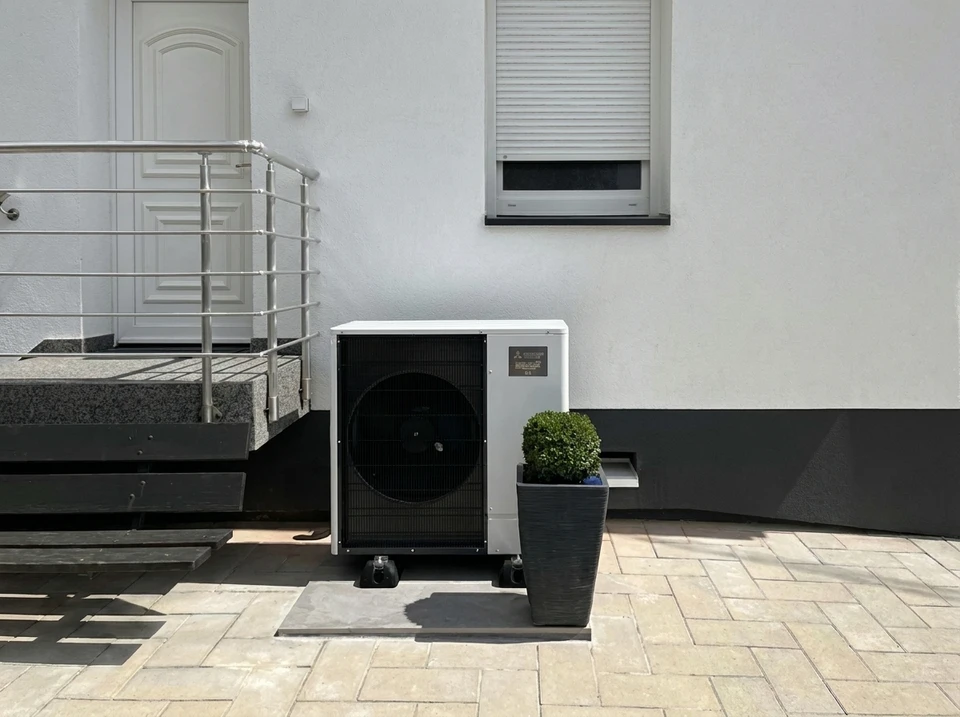Technicien en climatisation tenant des manomètres à l'extérieur devant une unité de climatisation résidentielle